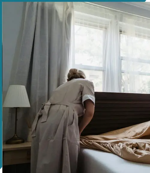 Zwei Hausangestellte machen ein Bett in einem sonnendurchfluteten Schlafzimmer und demonstrieren damit Sauberkeit und Liebe zum Detail.